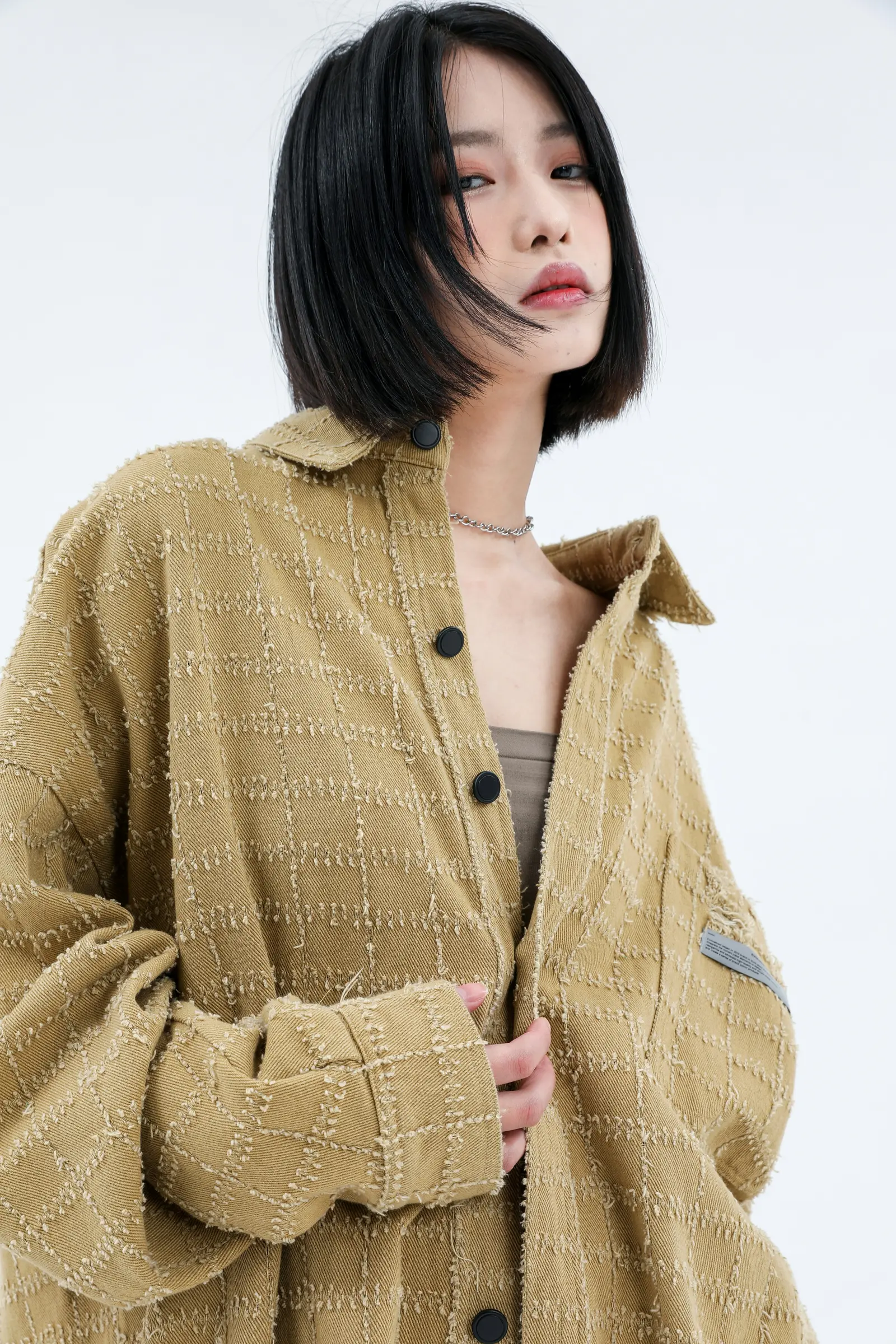Woman with a black bob haircut wearing a textured tan jacket