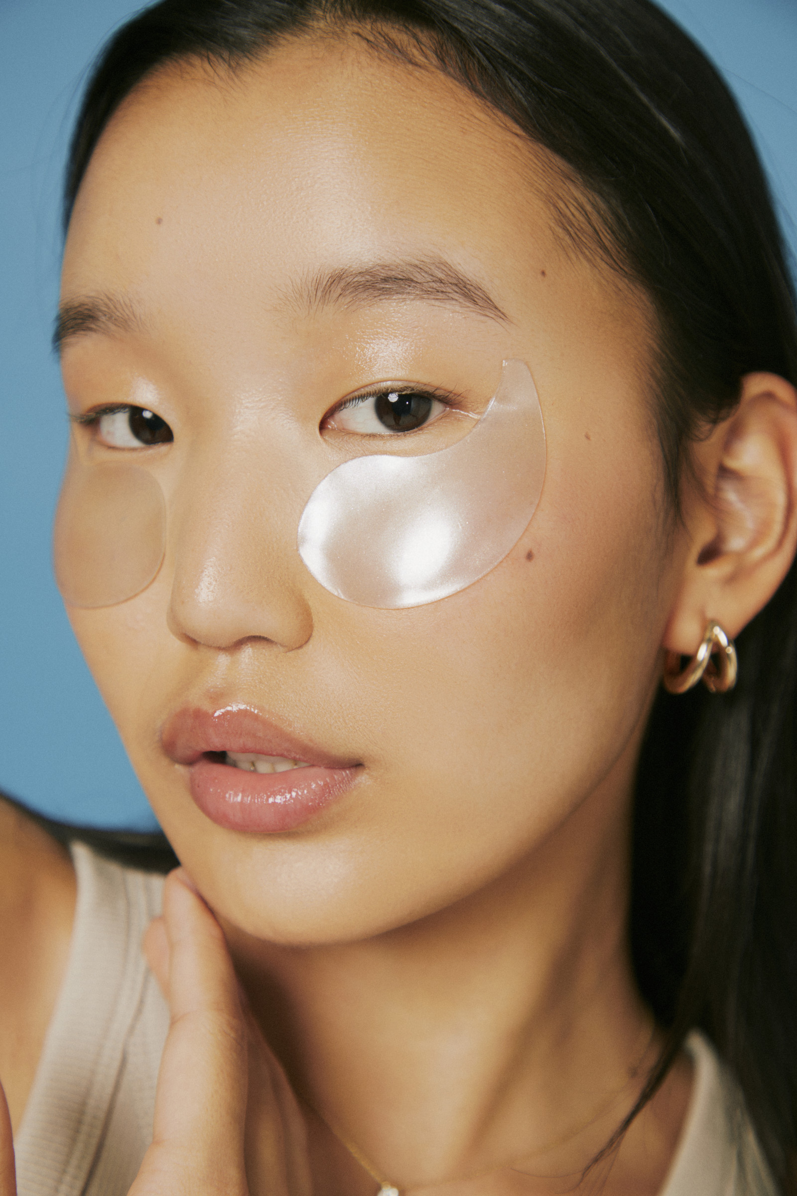 Close portrait of a woman wearing translucent under-eye patches against a blue background